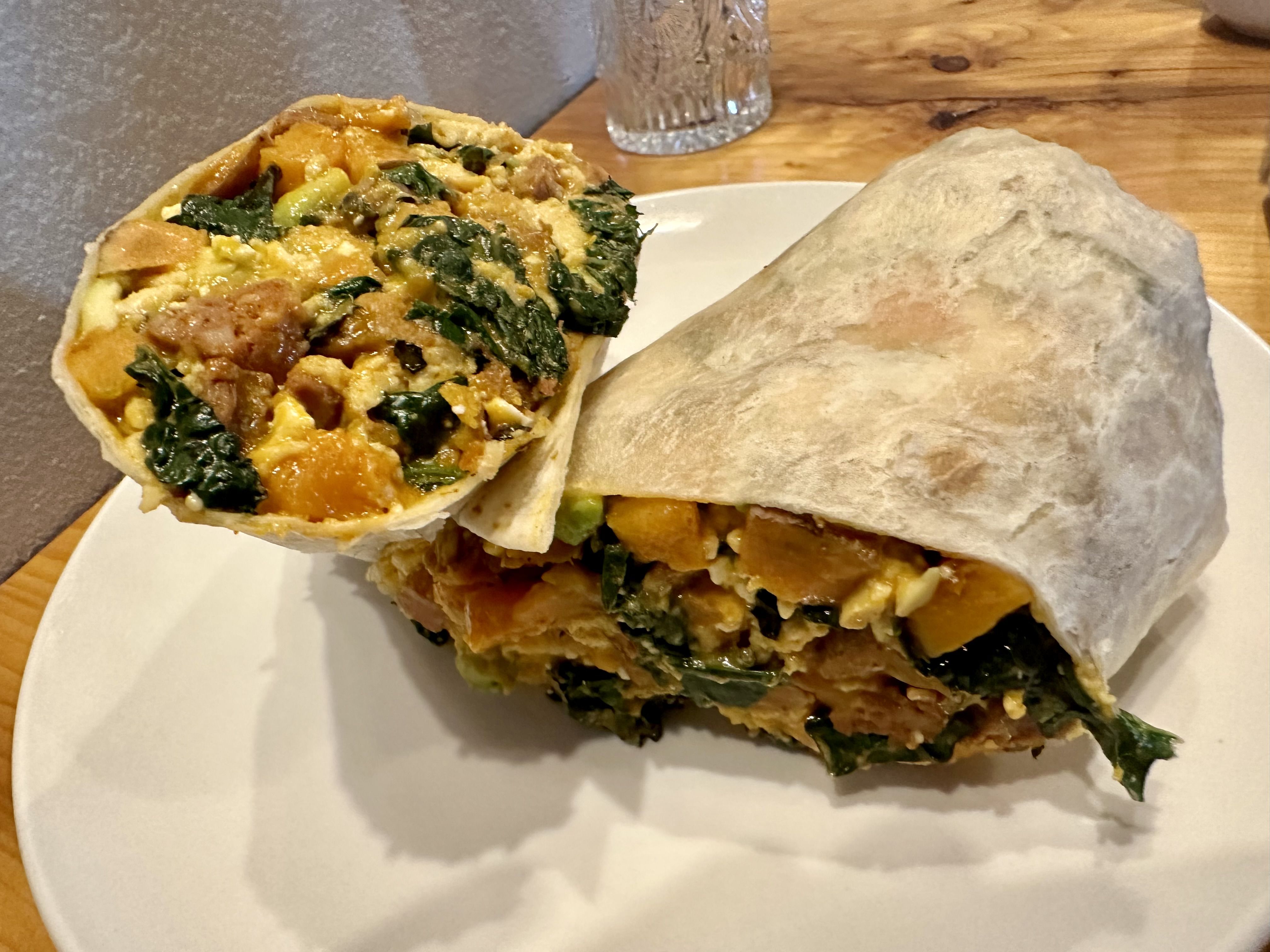 A burrito cut in half on a plate and filled with Kale, egg and sweet potato. 
