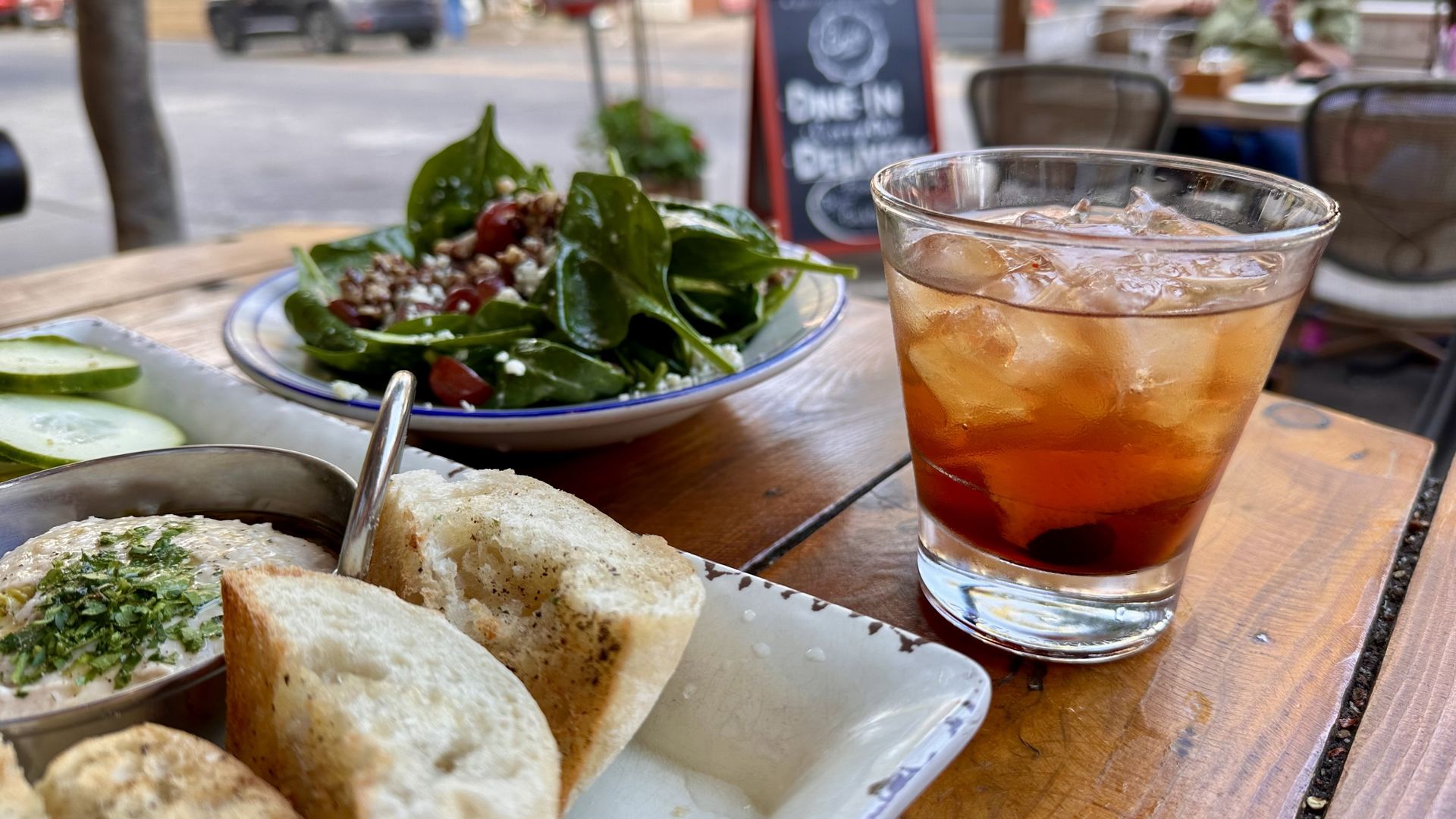 A photo of a tray of bread and dip, a salad in the background and a brownish colored drink