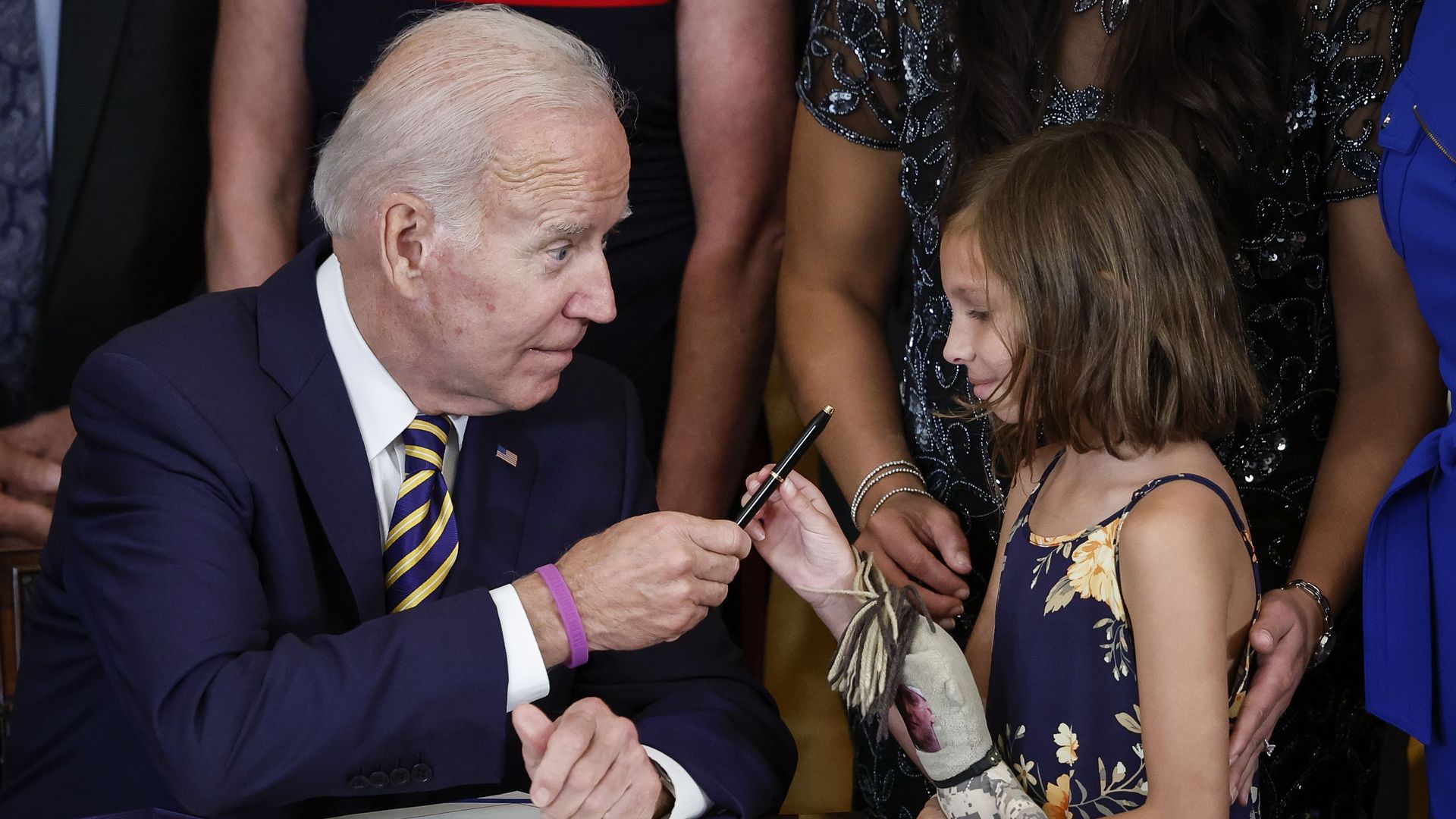 In the East Room yesterday, President Biden hands a pen to Brielle Robinson, daughter of the late Sgt. First Class Heath Robinson, after signing the PACT Act expansion of veterans' health benefits.