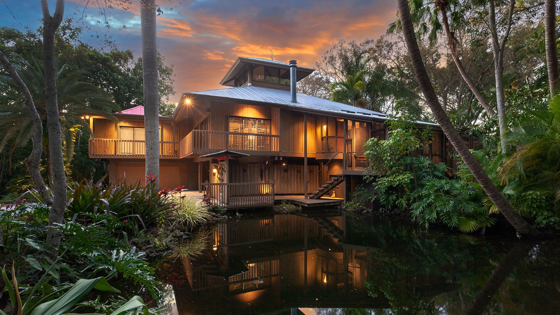 A house overlooking a pond a lush wetland greenery with a blue-and-pink sky overhead.