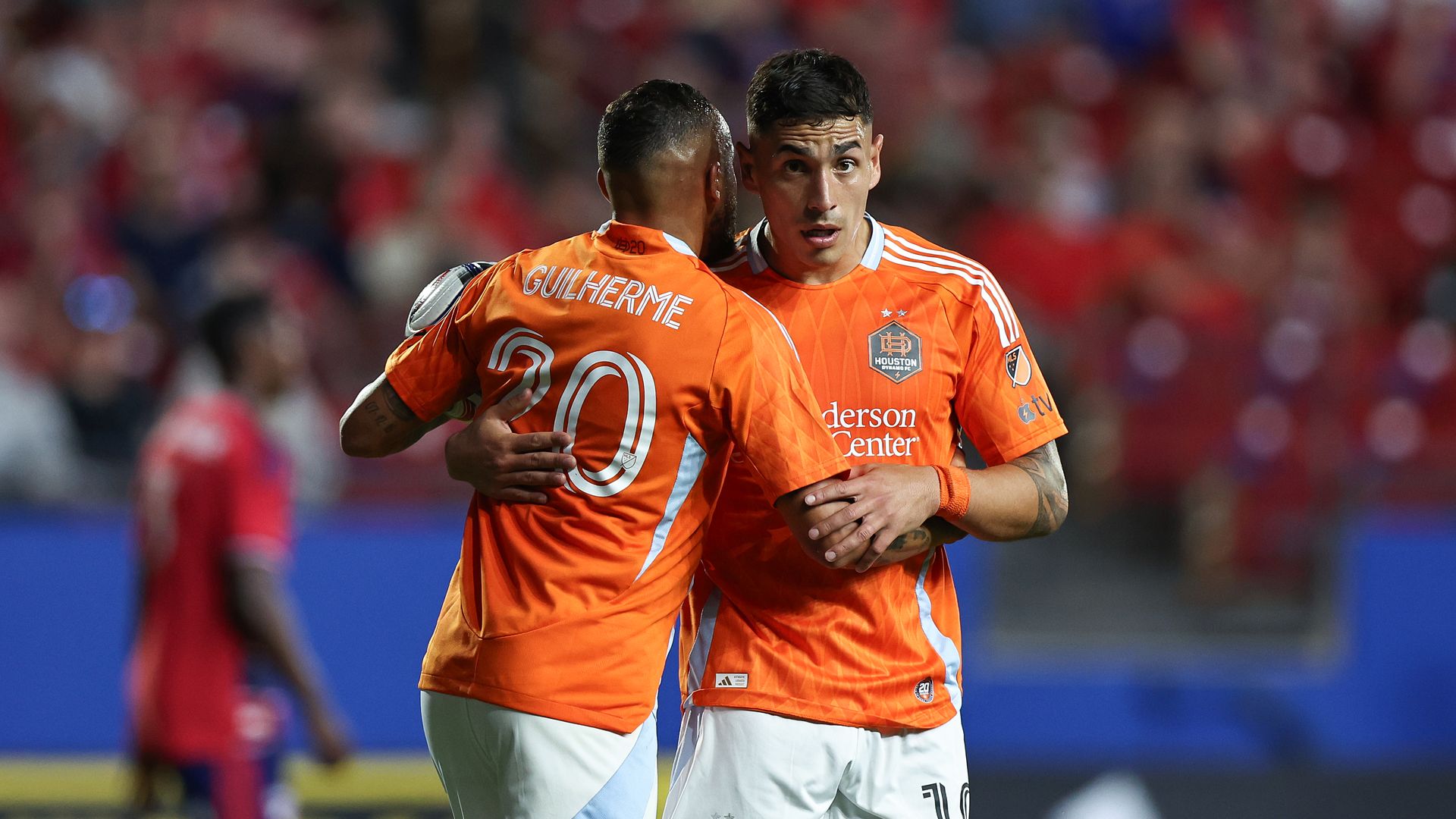 Dynamo players Guilherme and Ezequiel Ponce wearing orange jerseys and white shorts celebrate on the pitch