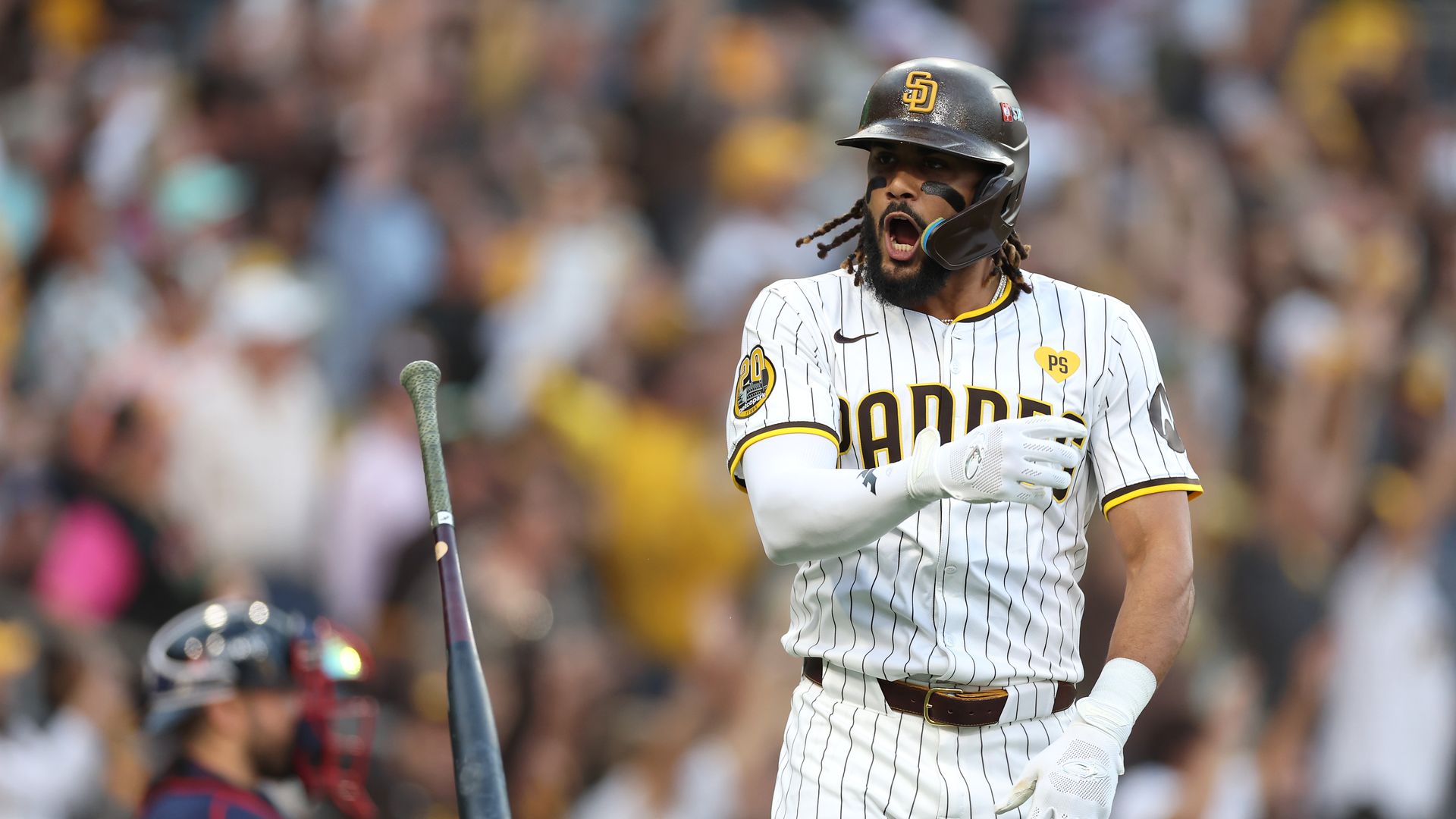 A man in a white pinstriped uniform tosses his bat and celebrates