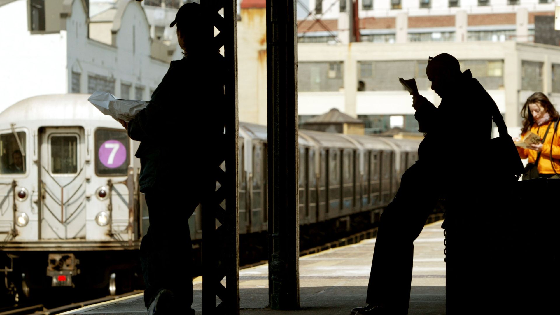A subway train travels above ground as commuters wait for a train.