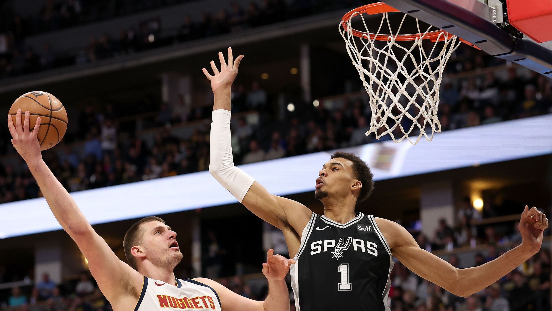 A basketball player shoots the ball over his opponent