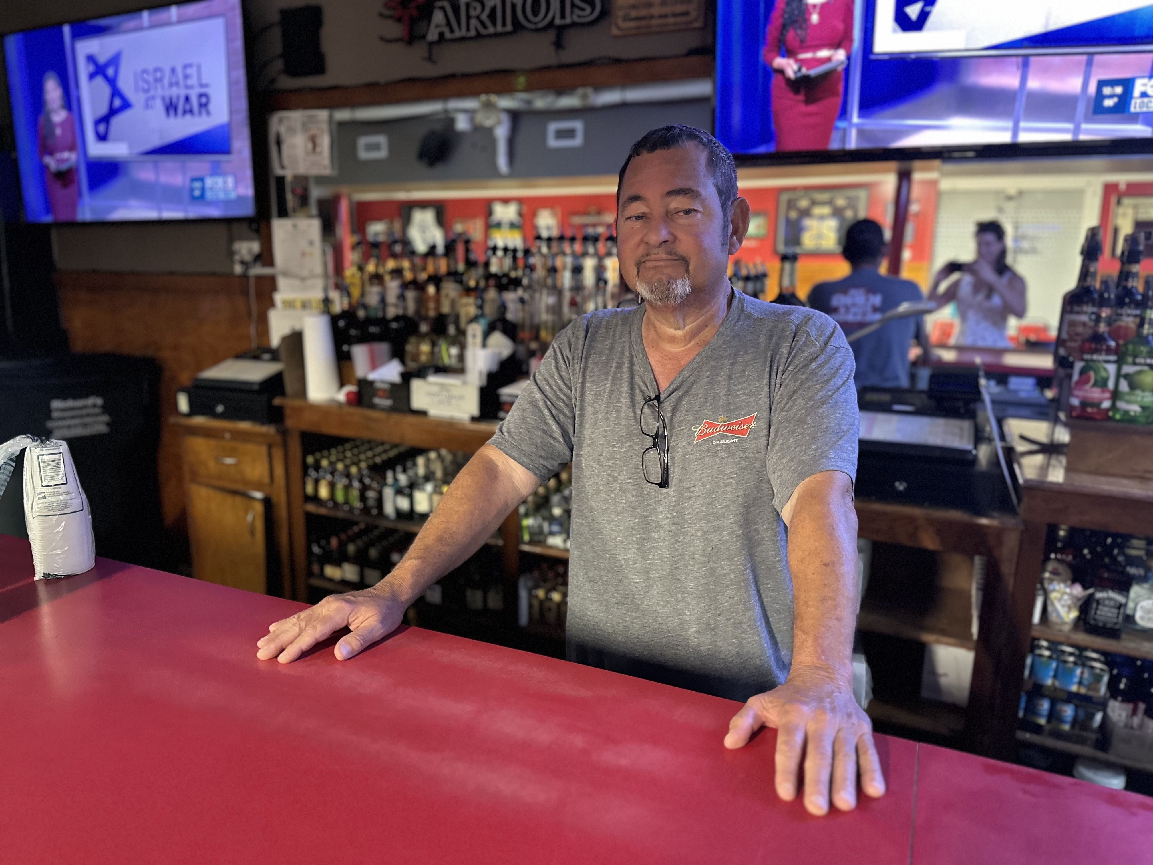 A man stands behind a red bar top and looks at the camera.