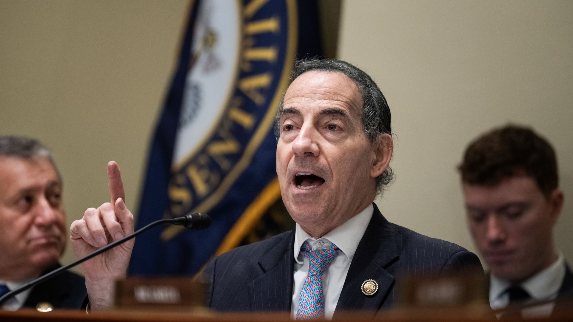 A man with dark hair who is wearing a dark suit and a colorful blue and red tie, Rep. Jamie Raskin, points as he speaks into a microphone during a congressional hearing.