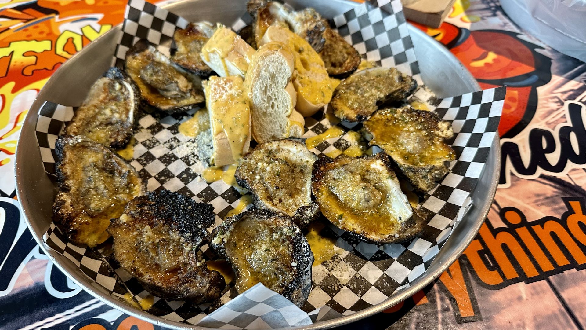 Photo shows a dozen chargrilled oysters on checked paper in a tray with garlic butter bread.
