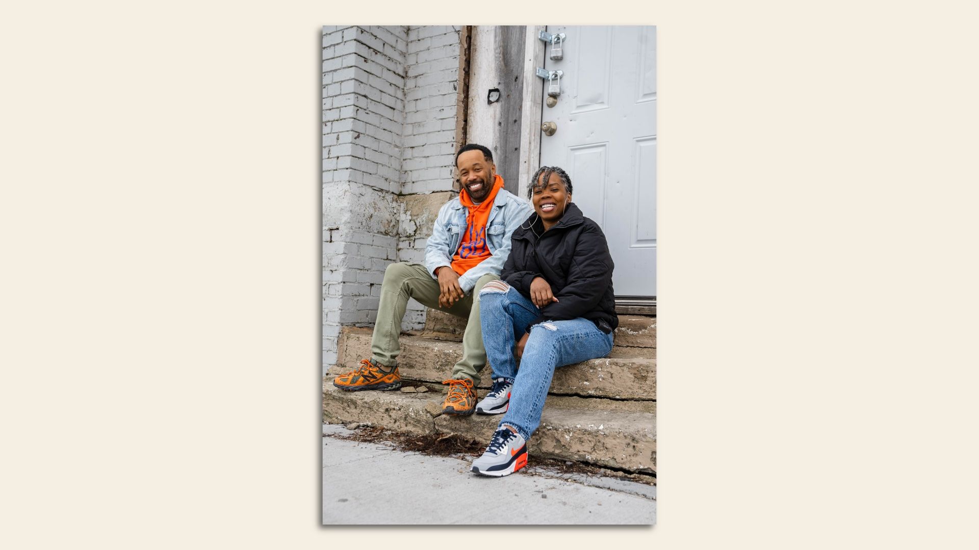 A man in orange hoodie sitting on concrete steps with a woman in a black fleece. 
