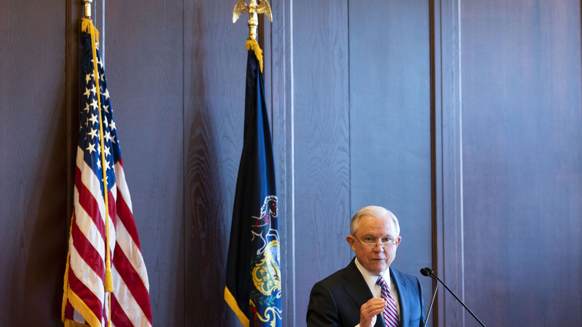 Jeff Session in front of a blue curtain and an American flag 