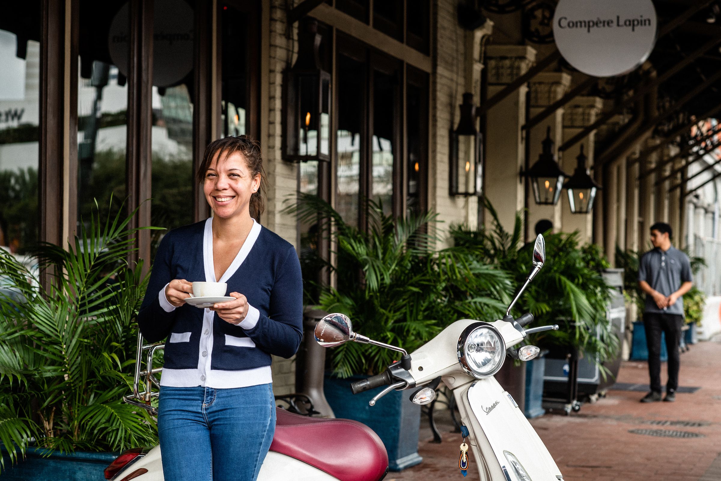 Photo shows Chef Nina Compton smiling and holding a coffee cup on the sidewalk outside Compere Lapin. 