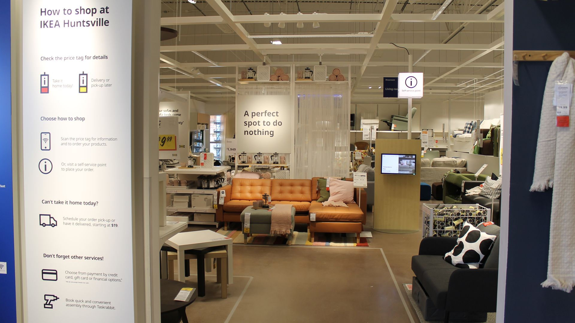 IKEA Huntsville showroom with a brown leather sectional sofa, a black chair with a polka dot pillow, and a sign reading "A perfect spot to do nothing" in a bright, modern store setting.