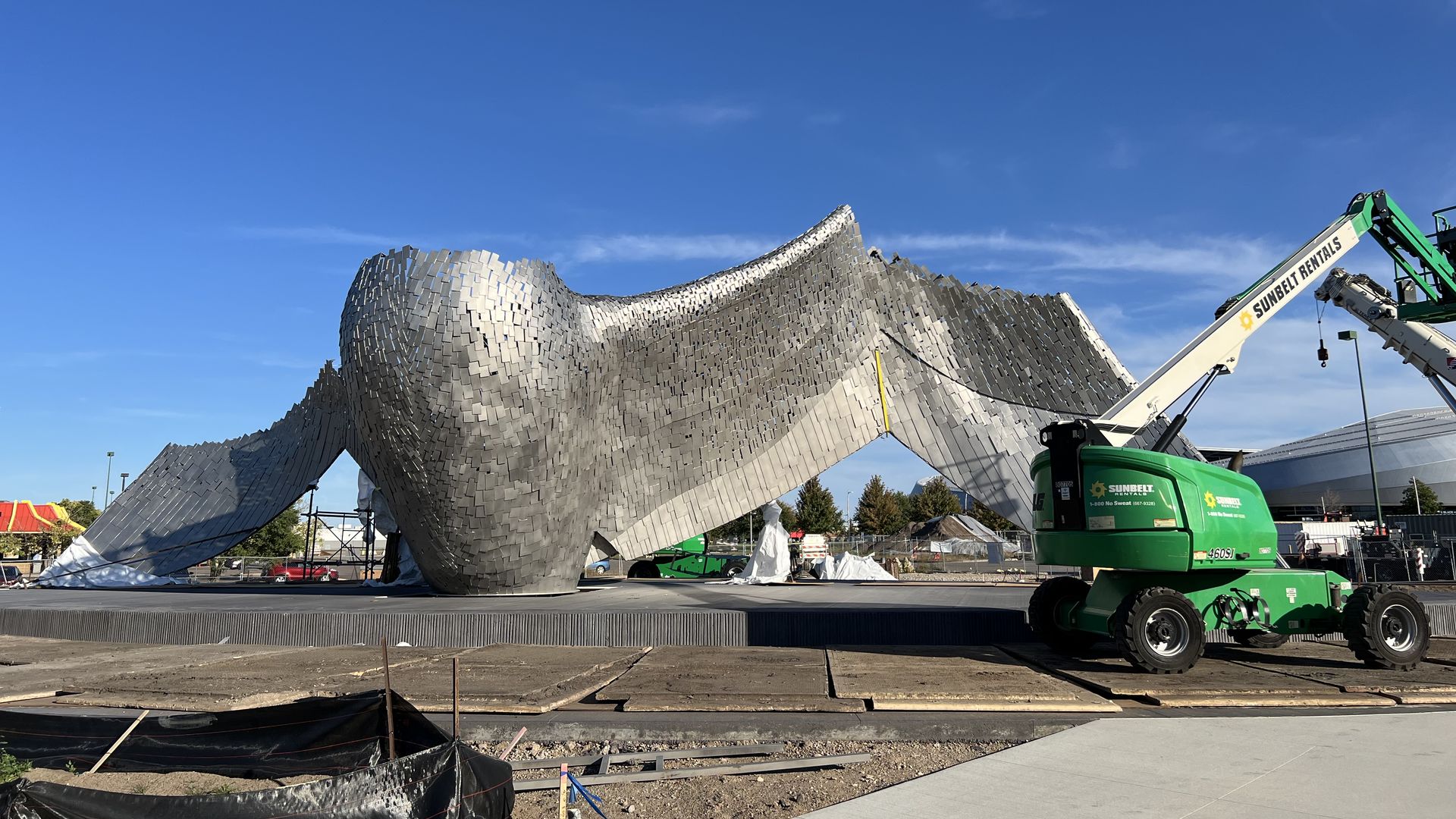 A giant sculpture of a bird made of metal rises out of a construction site with the shapes of wings and the breast of a bird visible, as if rising in flight out of a lake.