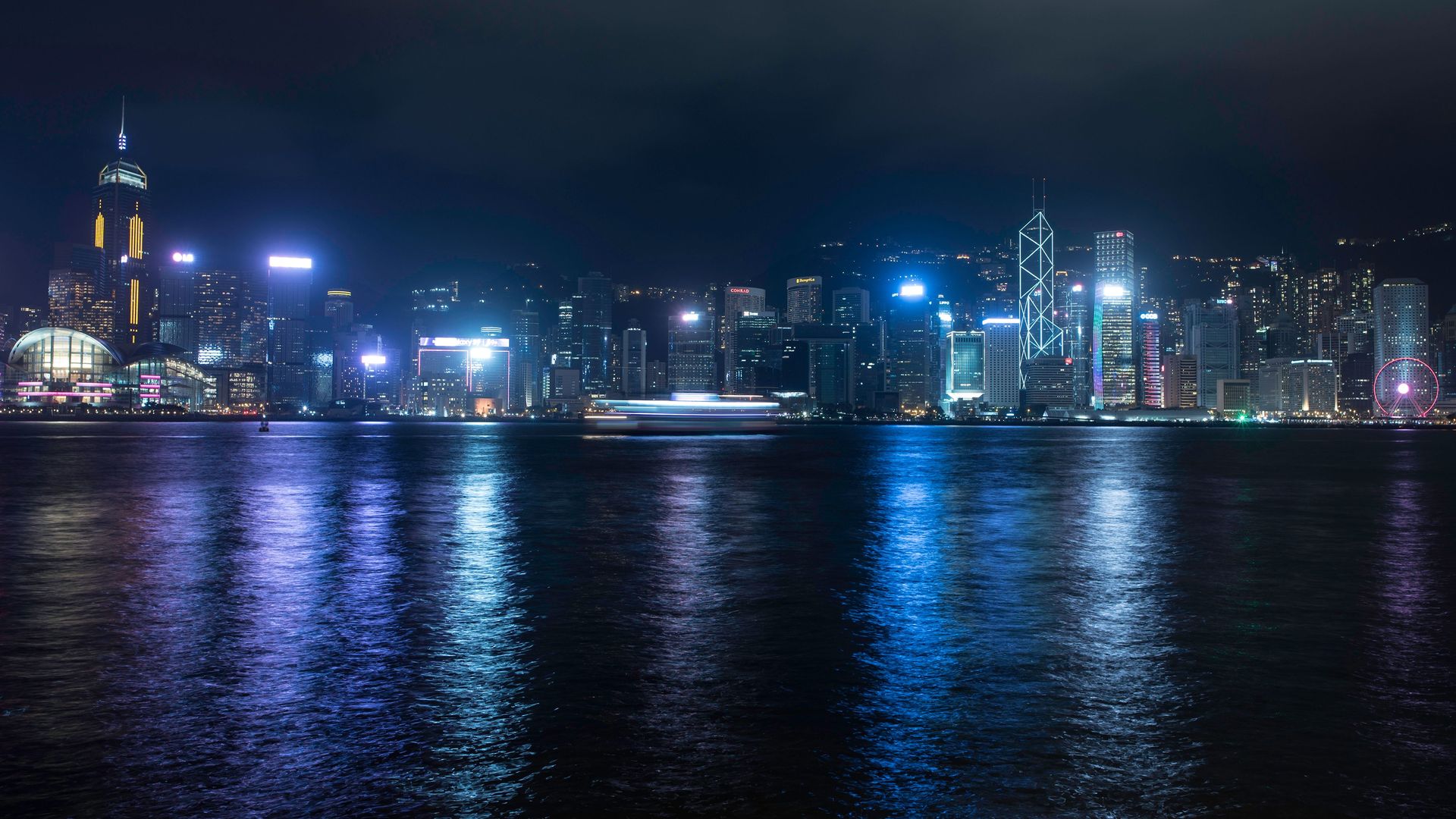 Hong Kong skyline in the dark with all the lights on. Everything has a neon blue hue in the darkness.