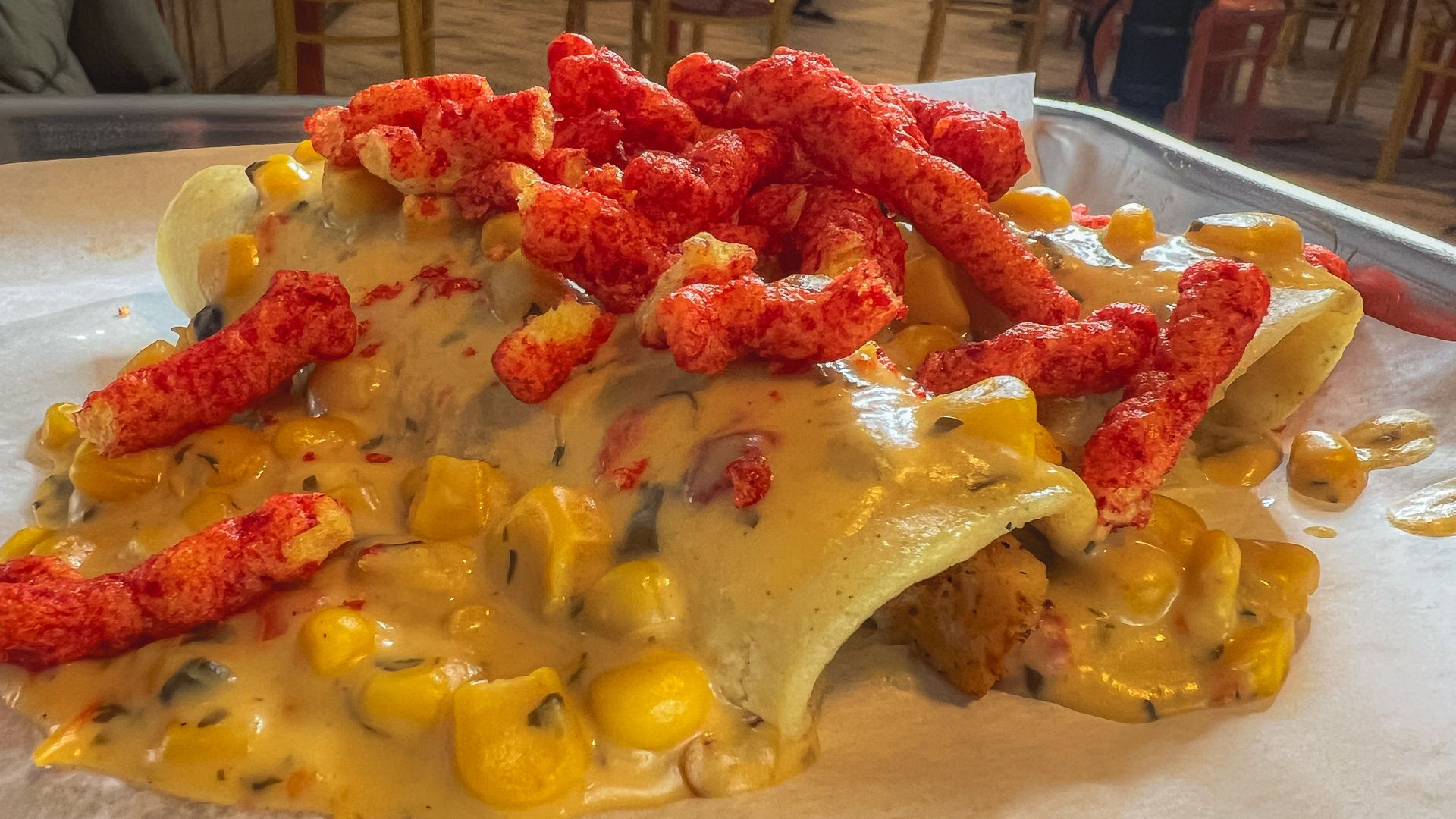 Two corn tortillas, stuffed with chicken, and topped with red chips, sauce and corn.