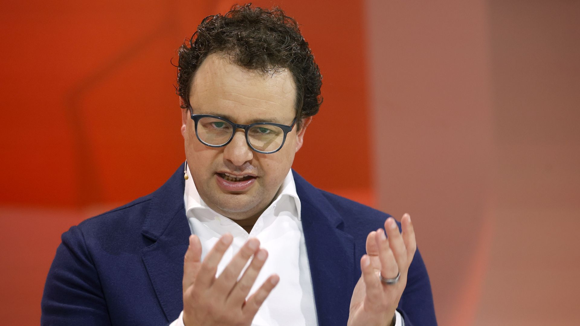 Dario Amodei, seated and gesturing with both hands in front of an orange background. 