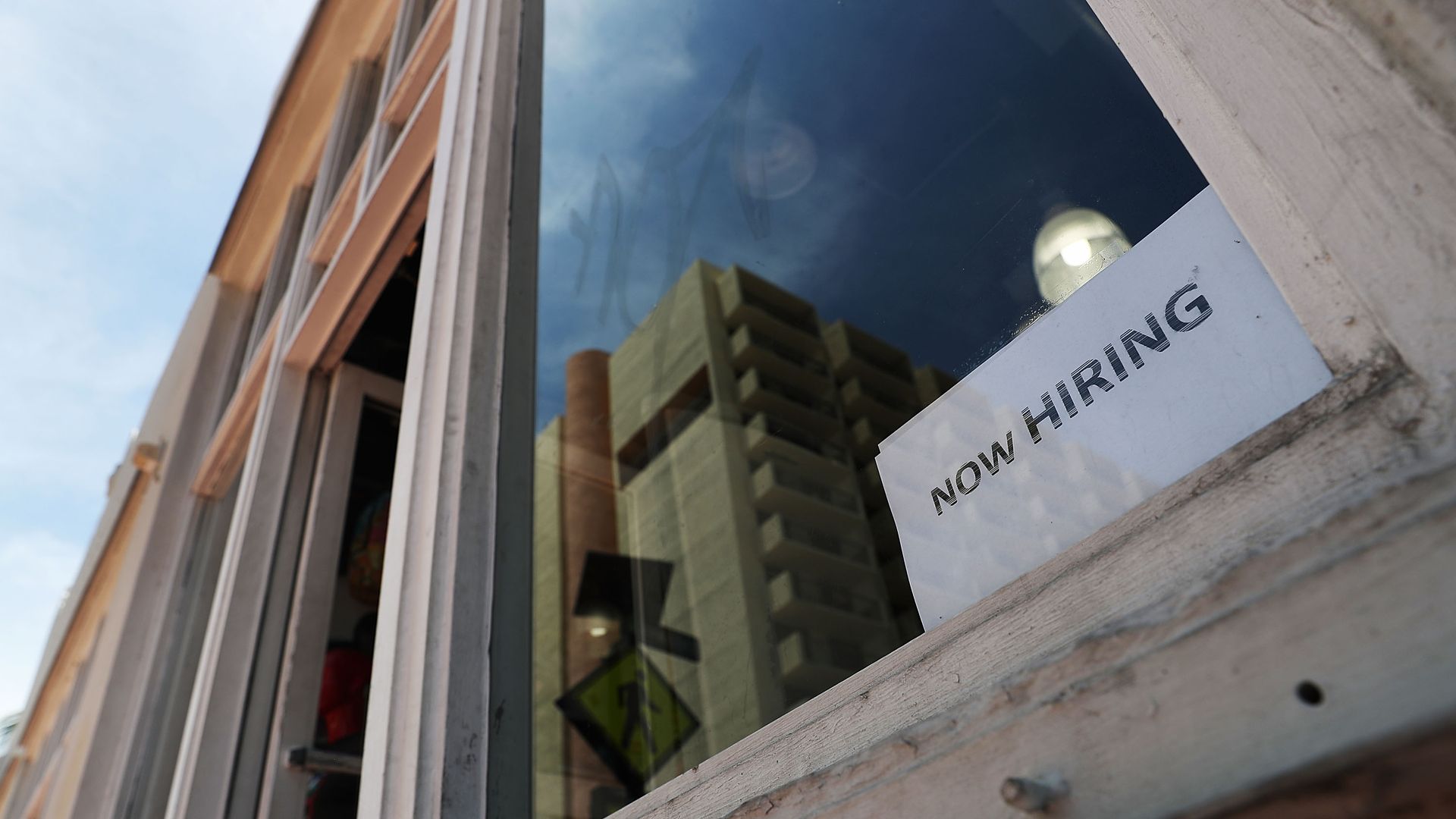 A simple "now hiring" sign in the window of a shop 