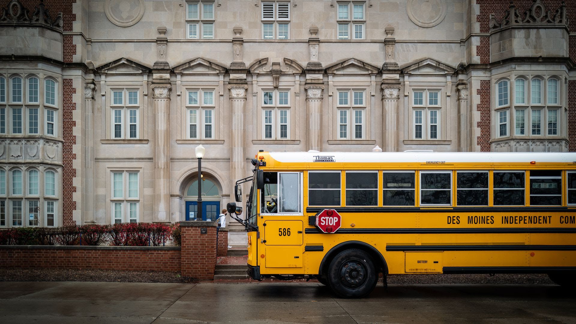 A Des Moines public school bus stops outside Roosevelt High School on an overcast day.