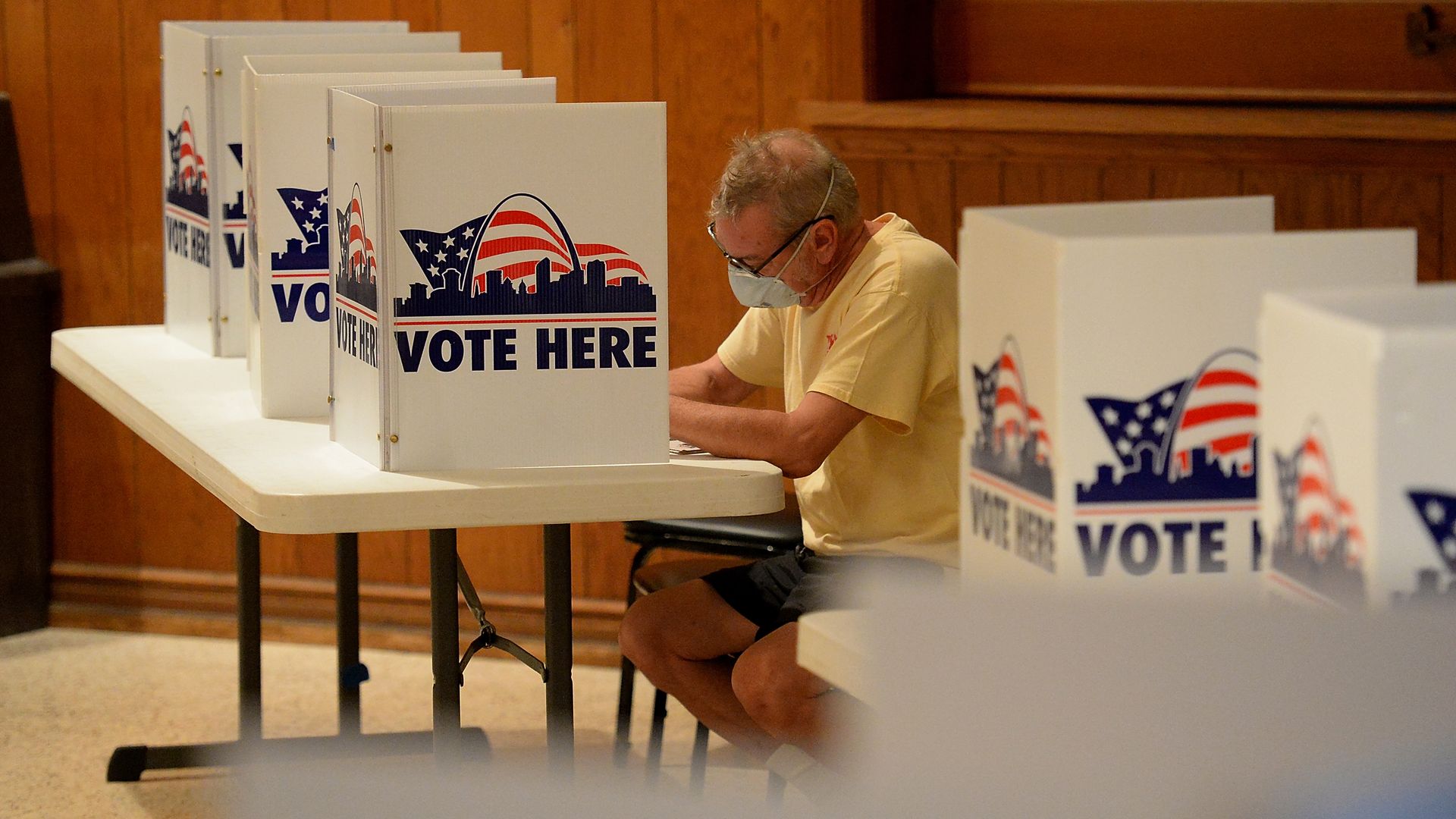 A man fills out his primary ballot while sitting down at a table with dividers