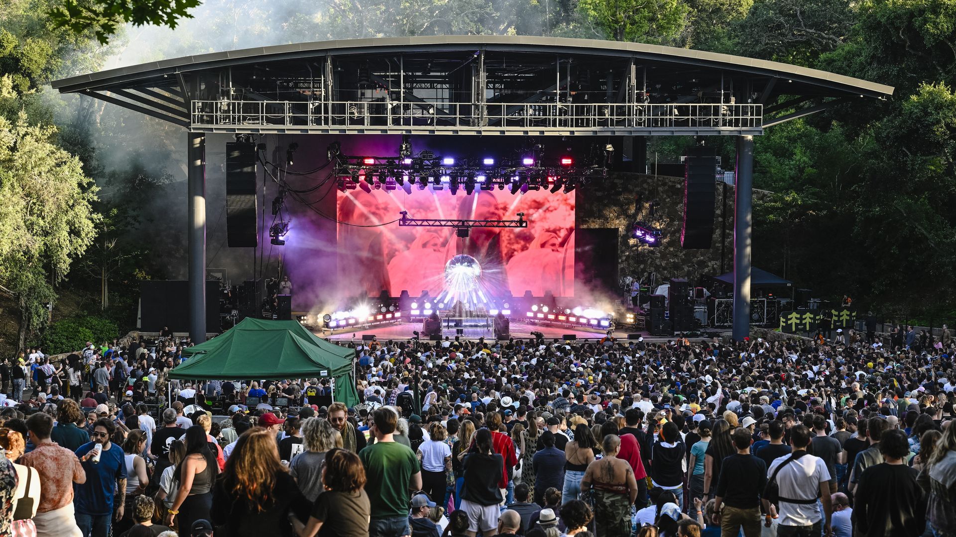 Photo of people crowded in an outdoor venue as they watch a smoke-filled music performance on stage