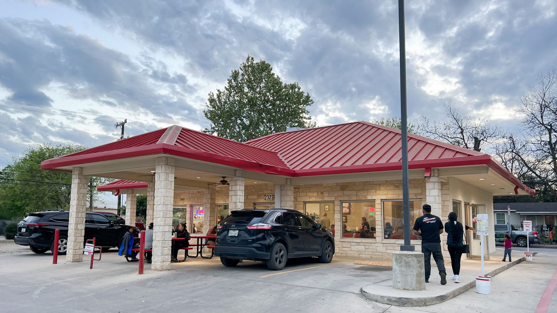 Customers walk into a brick restaurant with a metal red roof. 