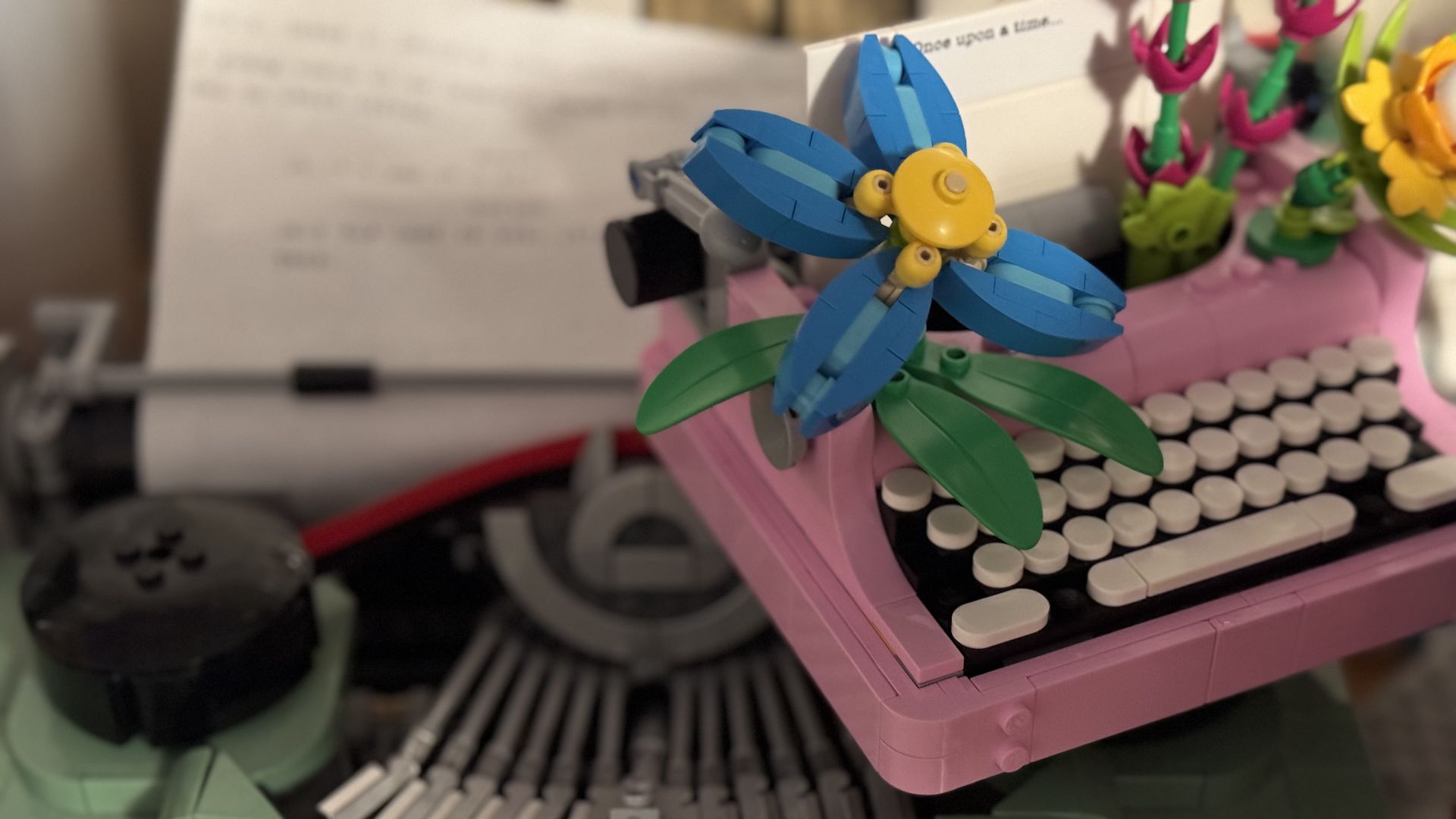 A small pink lego typewriter on top of a large green lego typewriter.