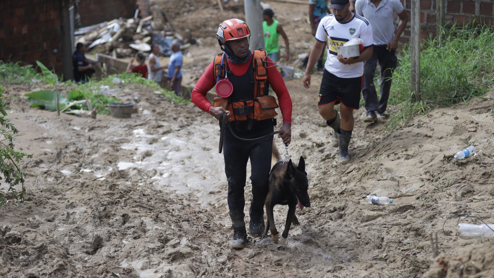 A rescuer wearing a red helmet walks with a search dog as they look for victims of a landslide in Brazil.
