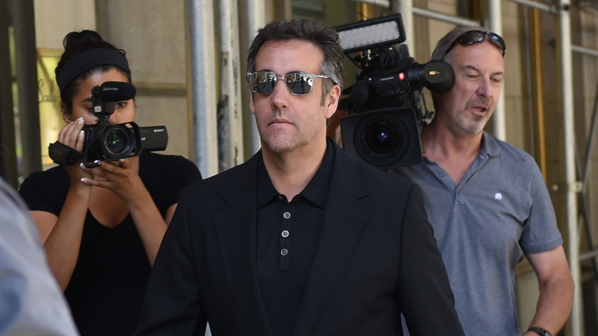 Michael Cohen walks down a sidewalk in sunglasses