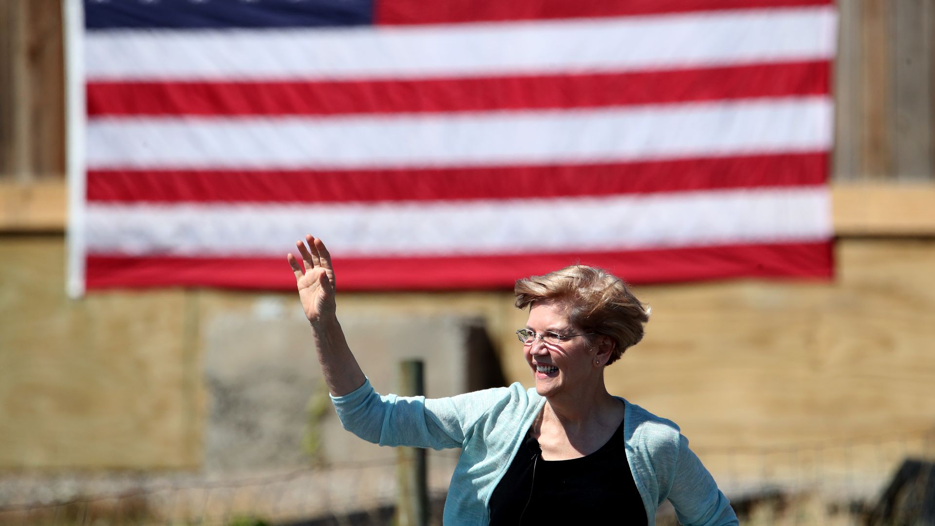 Elizabeth Warren waves in front of an American flag.