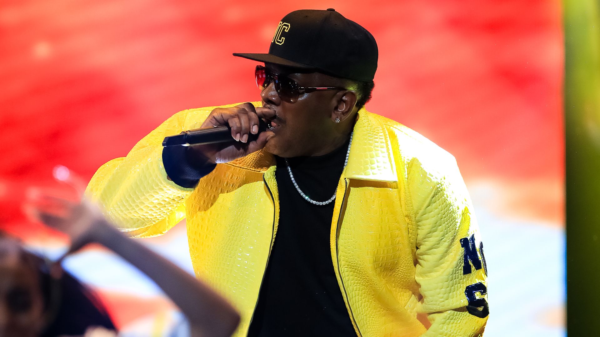 Petey Pablo perfomring in a yellow leather jacket in front of a red screen