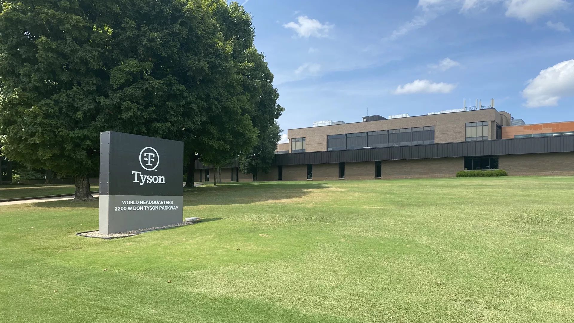 A photo of Tyson Foods' headquarters building and sign reading "Tyson" on a lush green lawn.