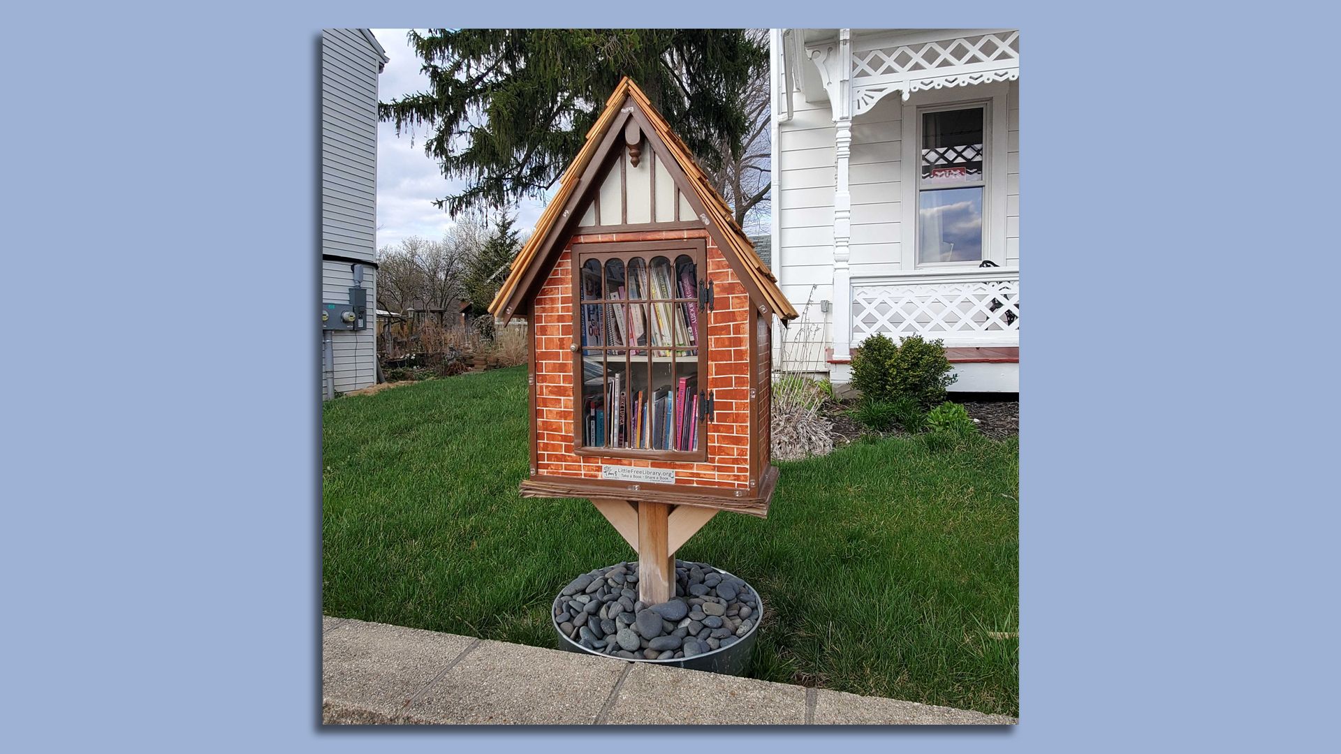 A "Little Free Library" in the shape of a miniature house next to a sidewalk.