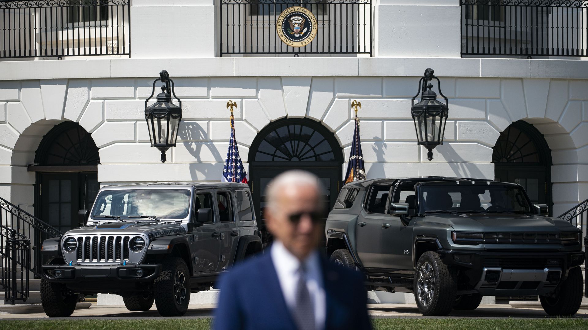 President Biden is seen in front of two cars during a clean-energy event on the White House South Lawn.