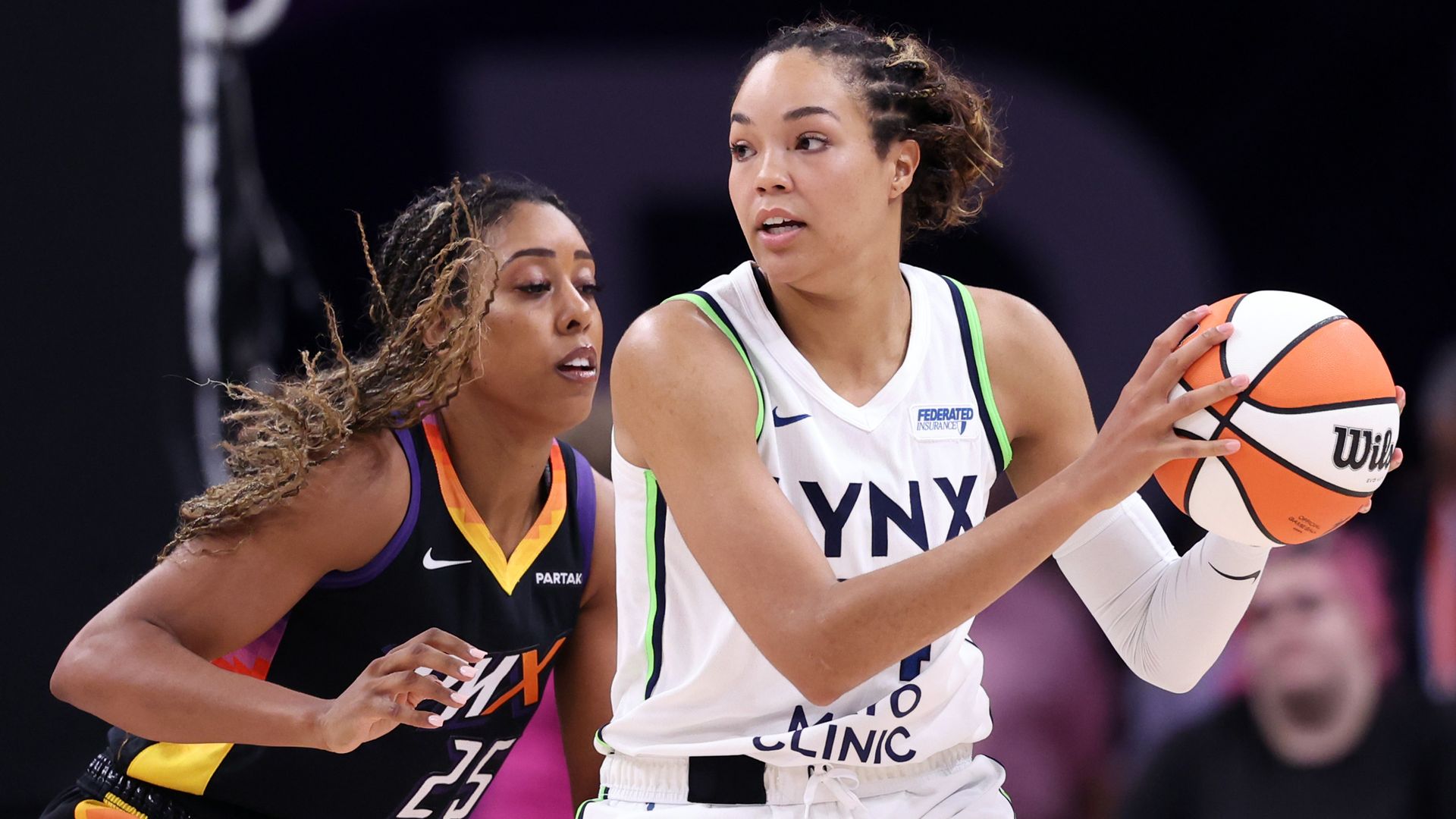 A photo pof Napheesa Collier holding a basketball while being guarded by a Phoenix player 