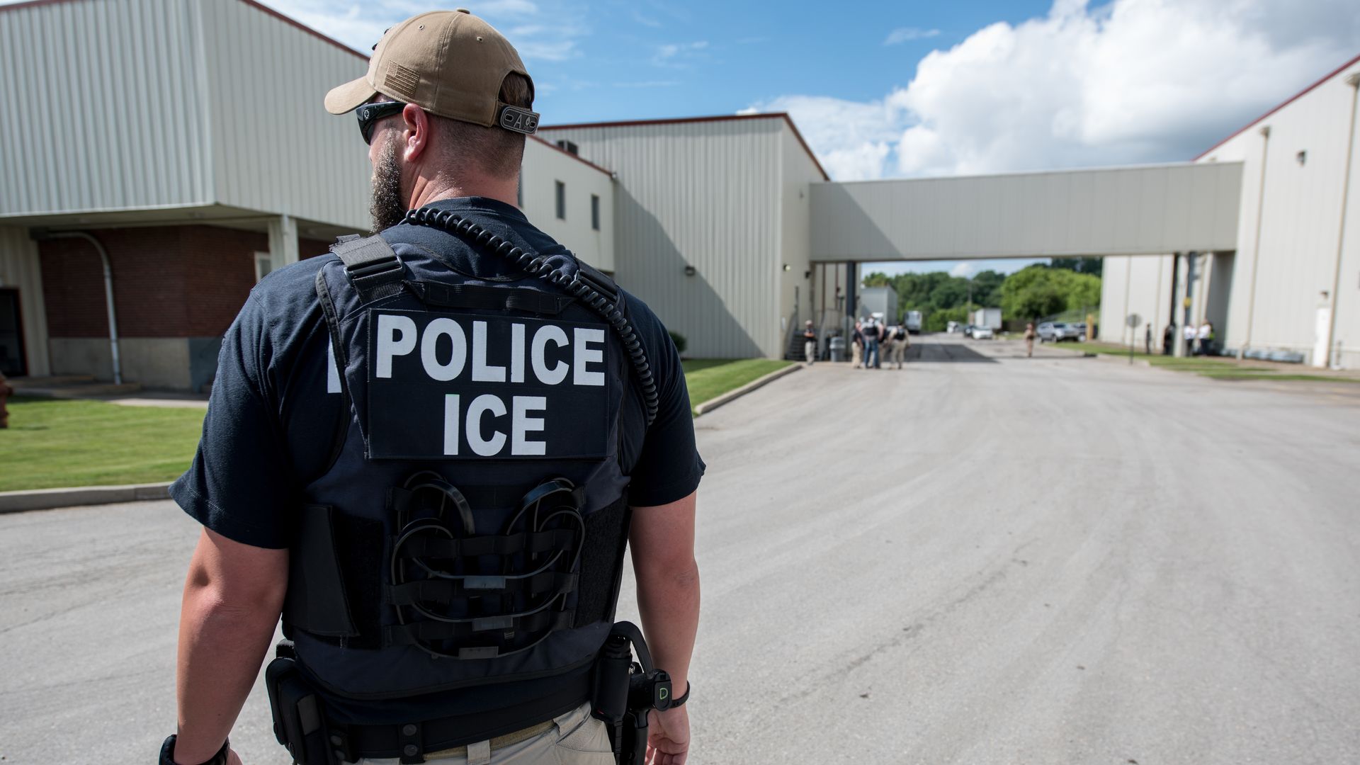 A white man with a hat and a vest that says "Police ICE" on it with his back to the camera.