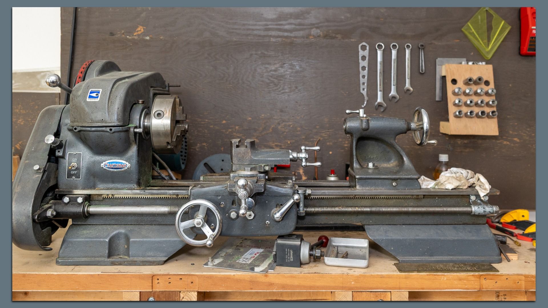 A vintage Craftsman metalworking lathe sits on a wooden workbench beneath an assortment of wrenches and other tools.