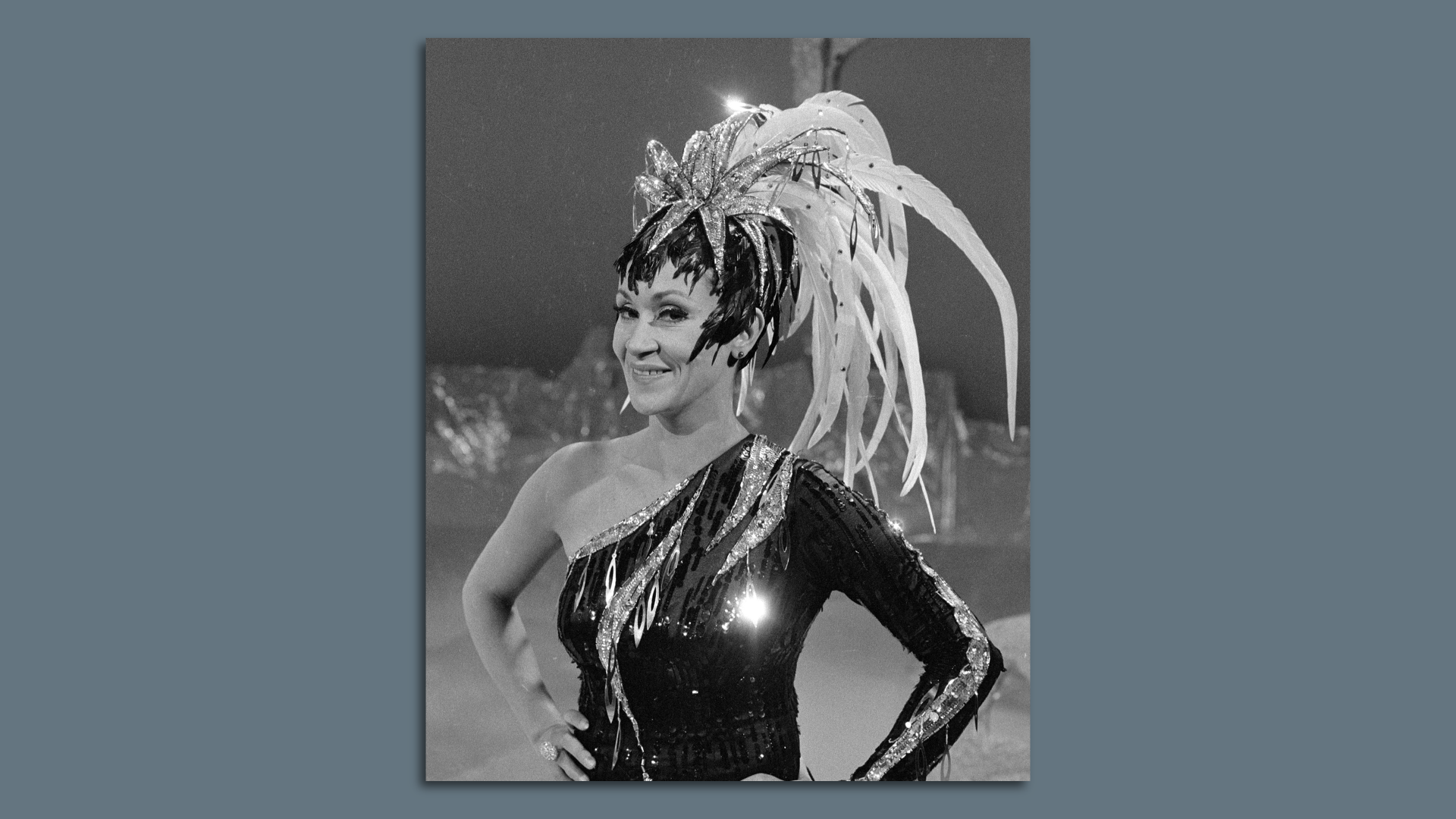 Chita Rivera poses with her hands on her waist, wearing a big feathered headdress