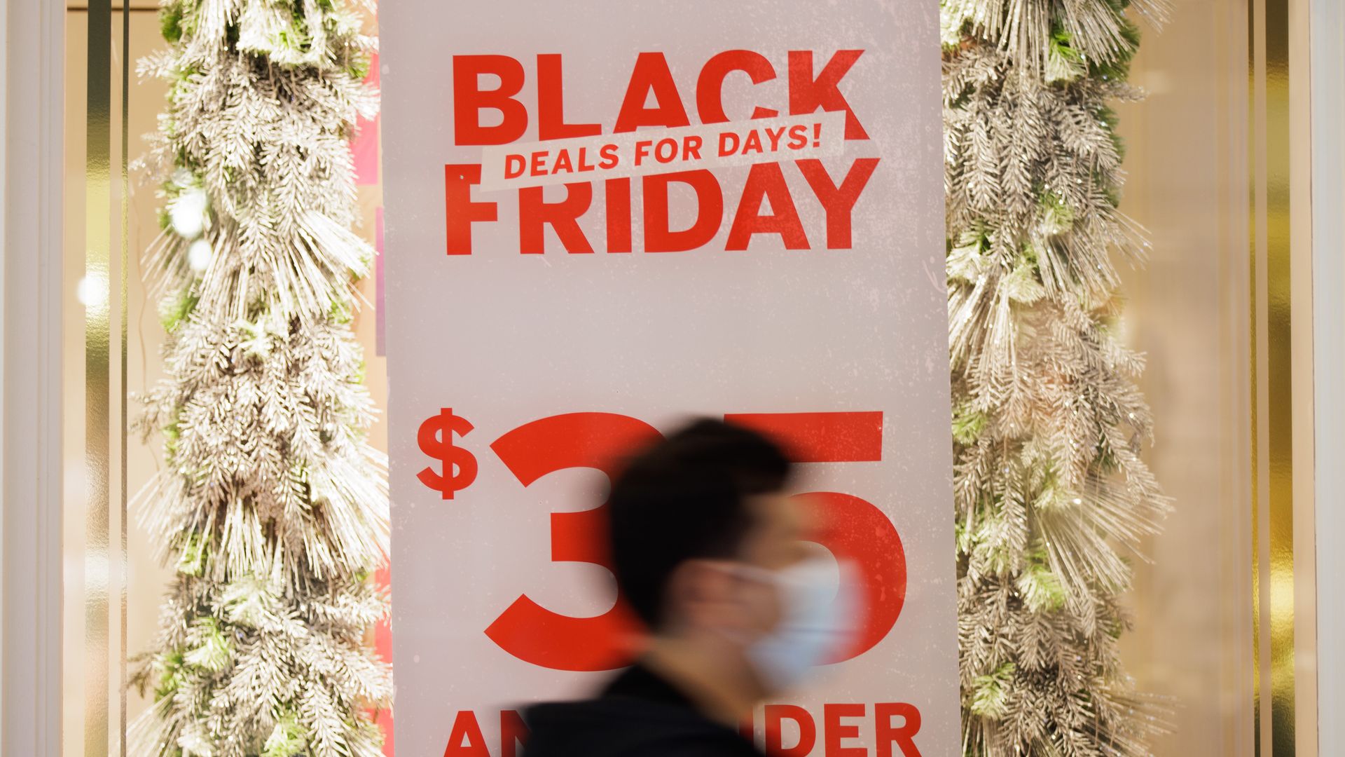 Shopper wearing a mask walks by a sign that says "Black Friday deals for days."
