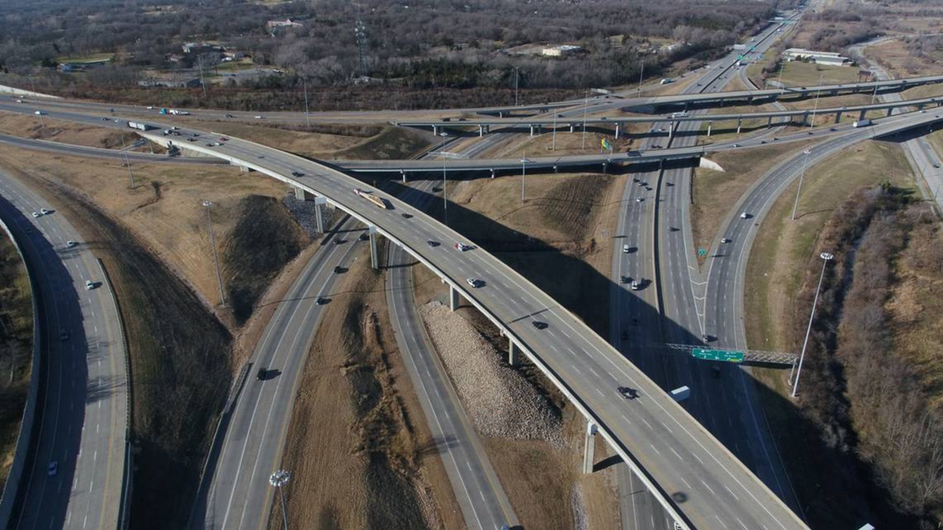 Aerial photo shows crisscrossing interstates with green signs and cars and trucks against brownish grass.