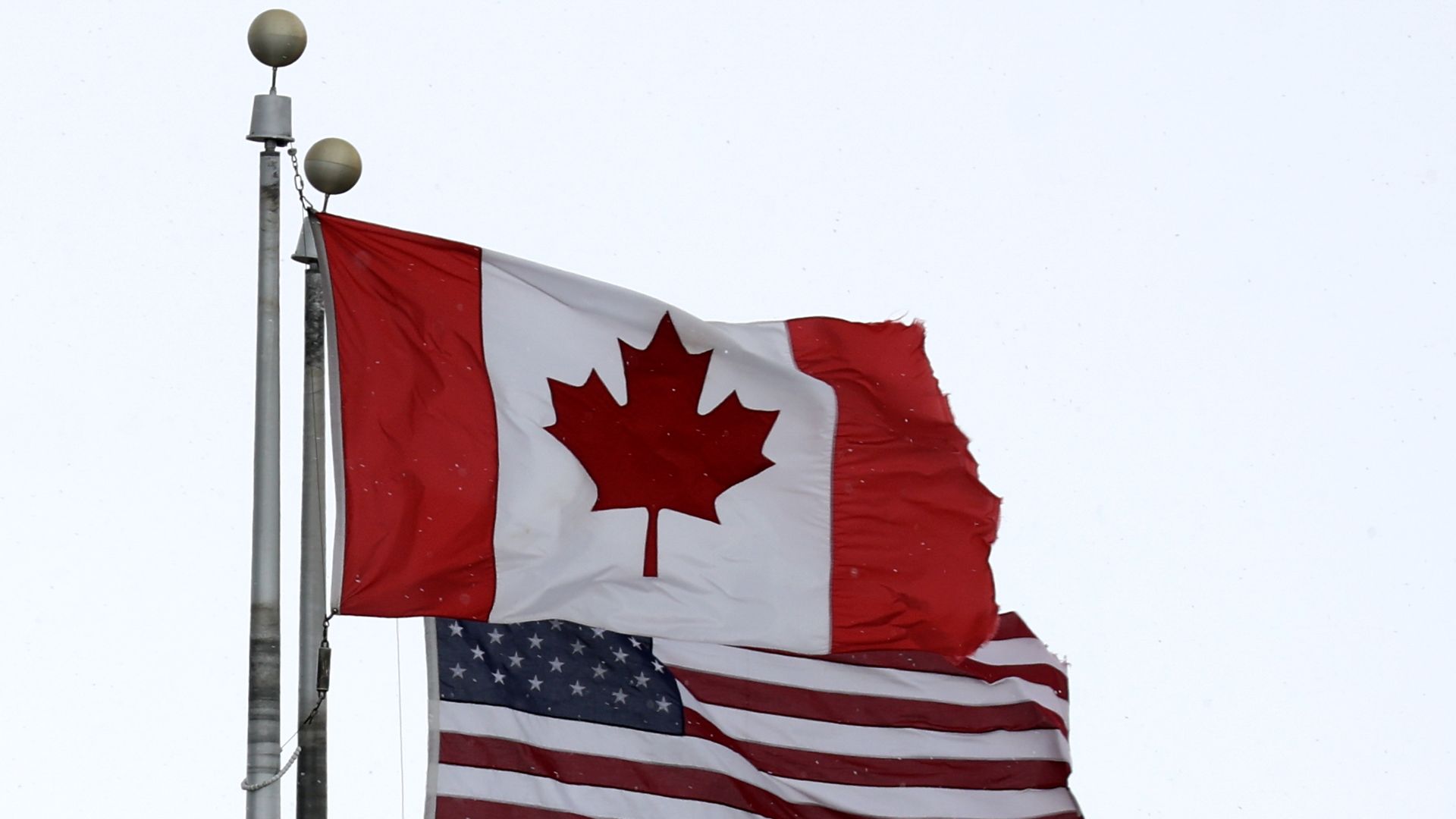 The Canadian flag flies next to the American flag on an overcast day