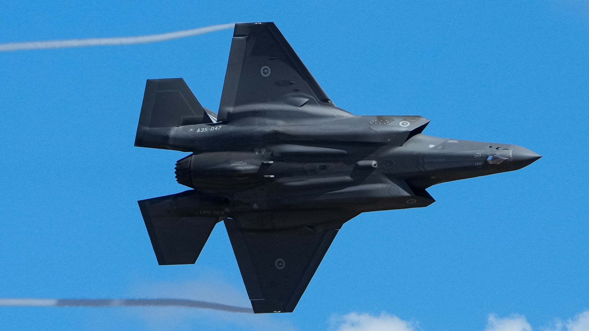 An F-35 flies in a blight blue sky.