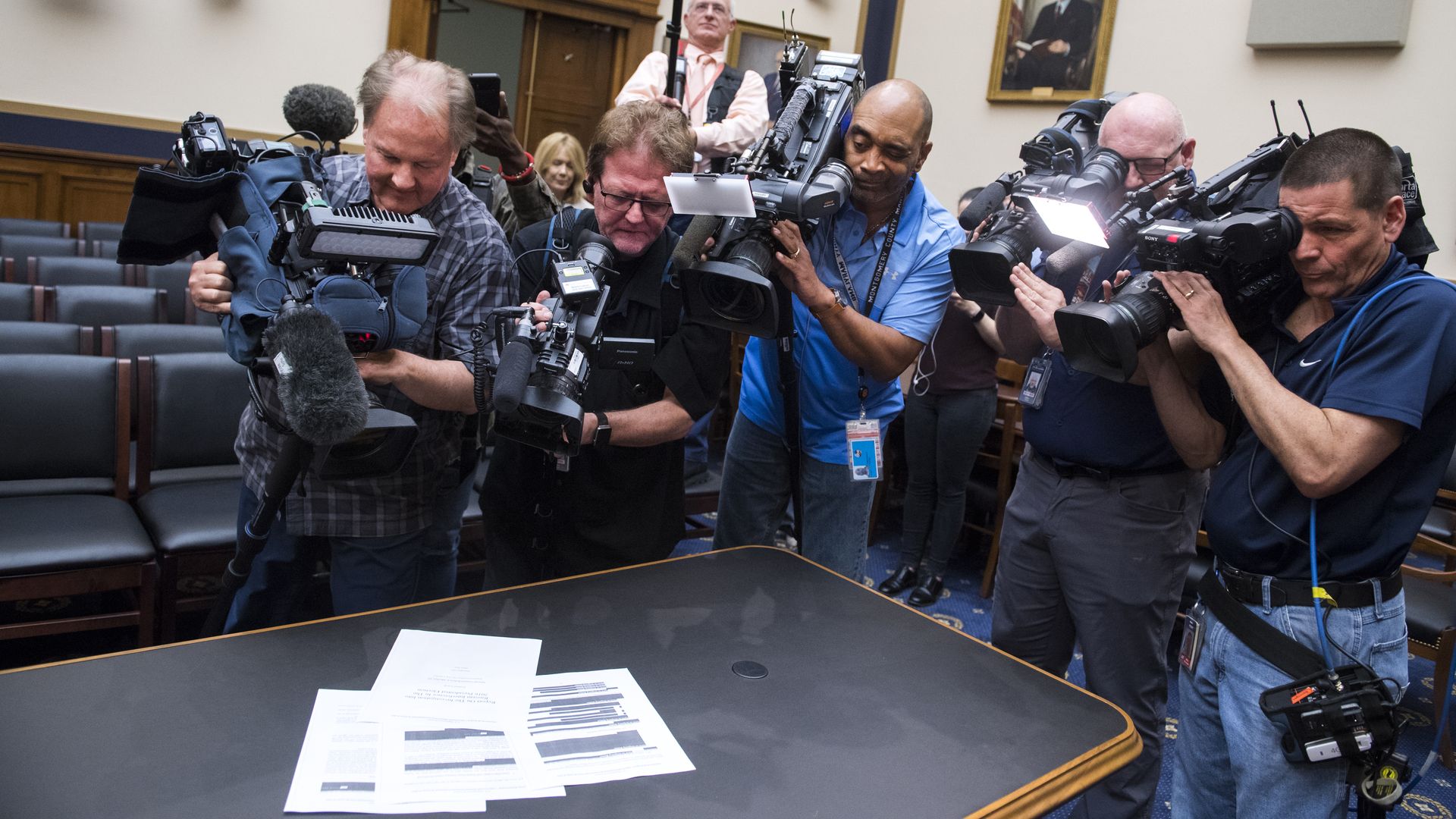 In this image, a crowd of reporters with cameras take pictures of papers in the Mueller report as it sits on a table.