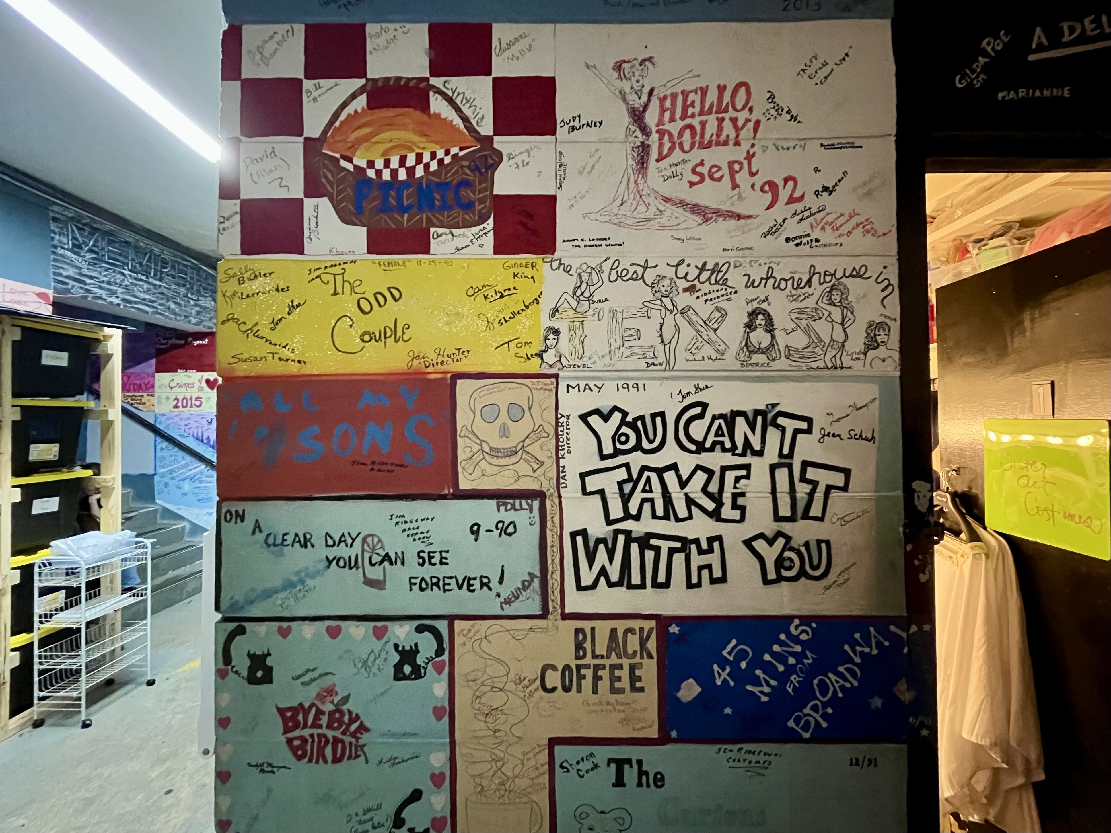 A wall with cinderblocks painted with names of various plays and musicals. Among them: "You Can't Take it With You," "Hello Dolly," and "Bye Bye Birdie."