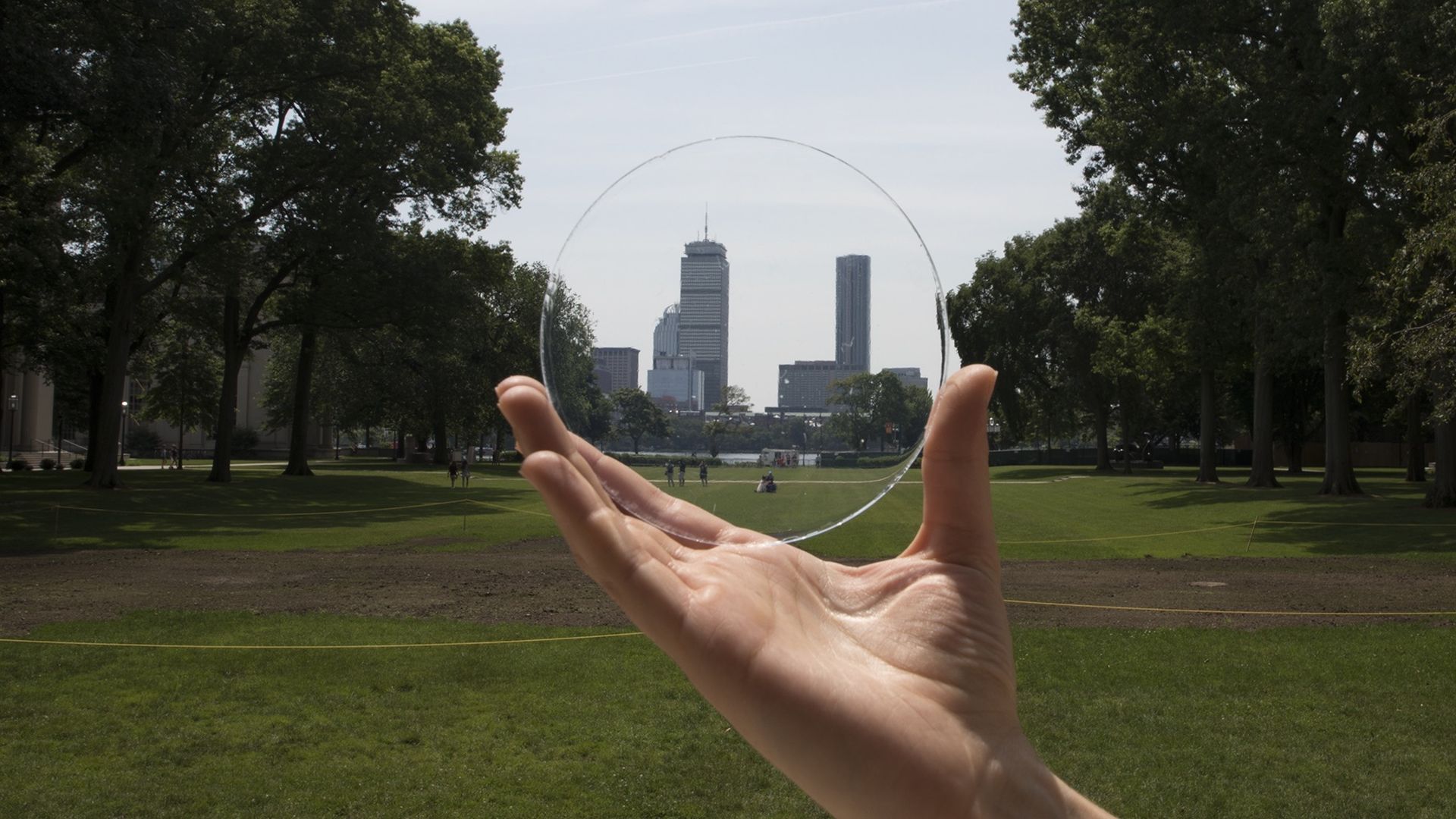 A circular slice of transparent aerogel is held in front of the Boston skyline.