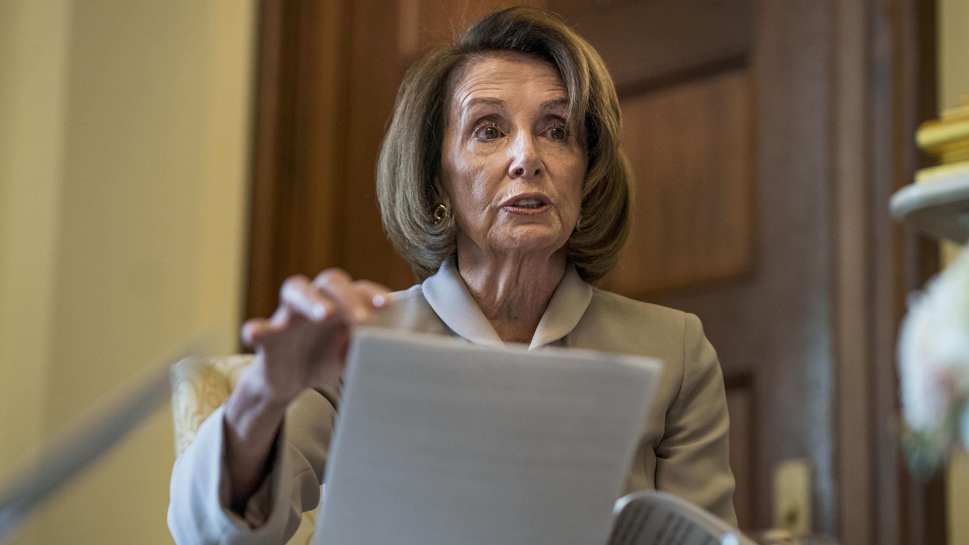 Nancy Pelosi holding a few sheets of paper while sitting