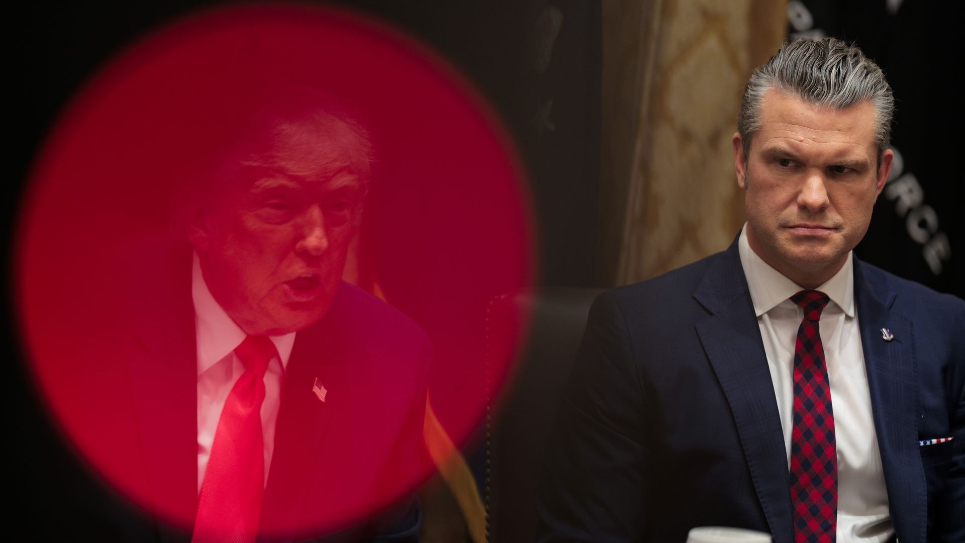 Man in a navy suit and red-checkered tie (Hegseth) sits with a serious expression next to a blurred image of another man wearing a red tie, partially obscured by a red circle (Trump).