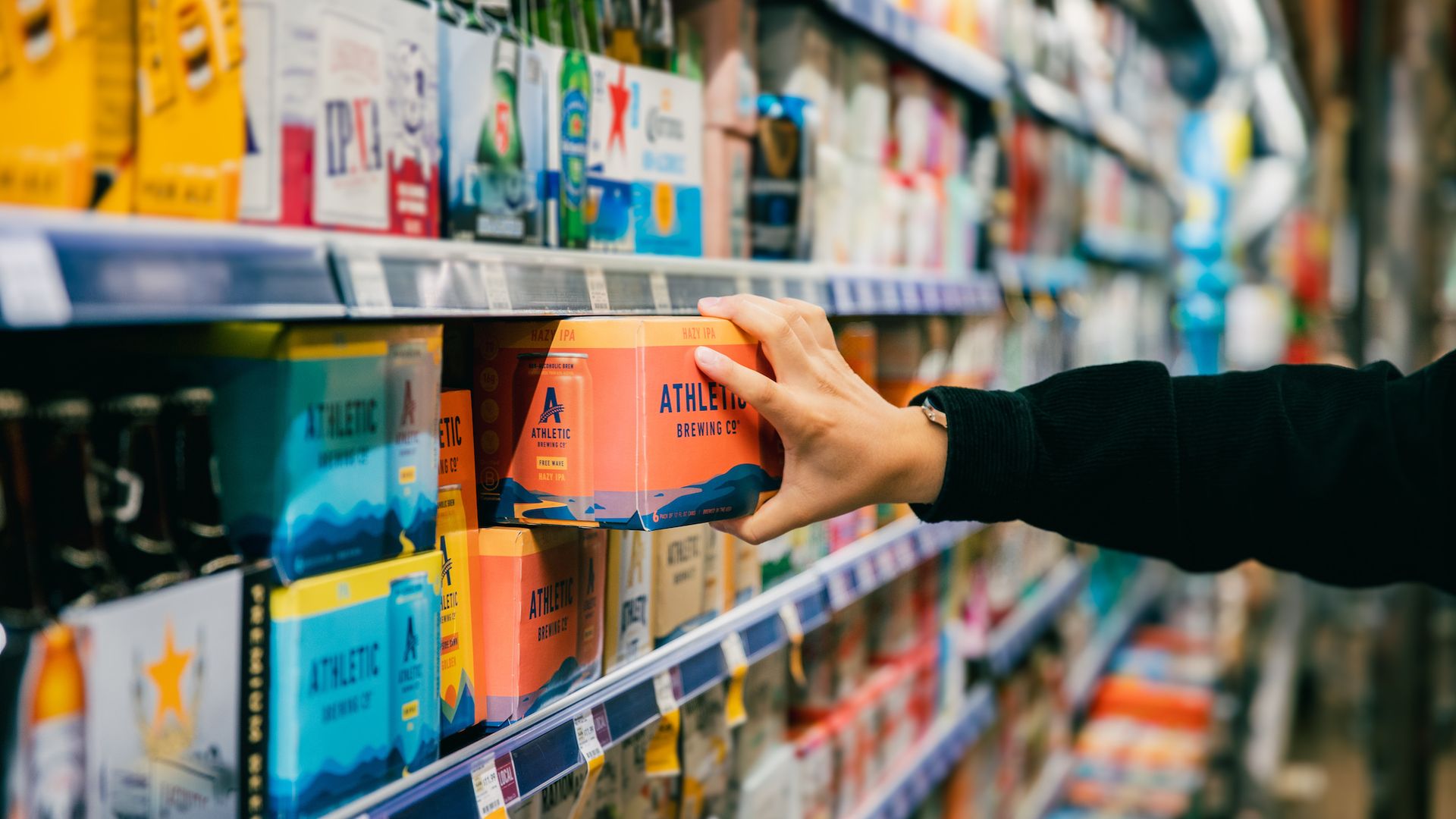 A hand pulls a case of Athletic beer from the shelf at a grocery store.