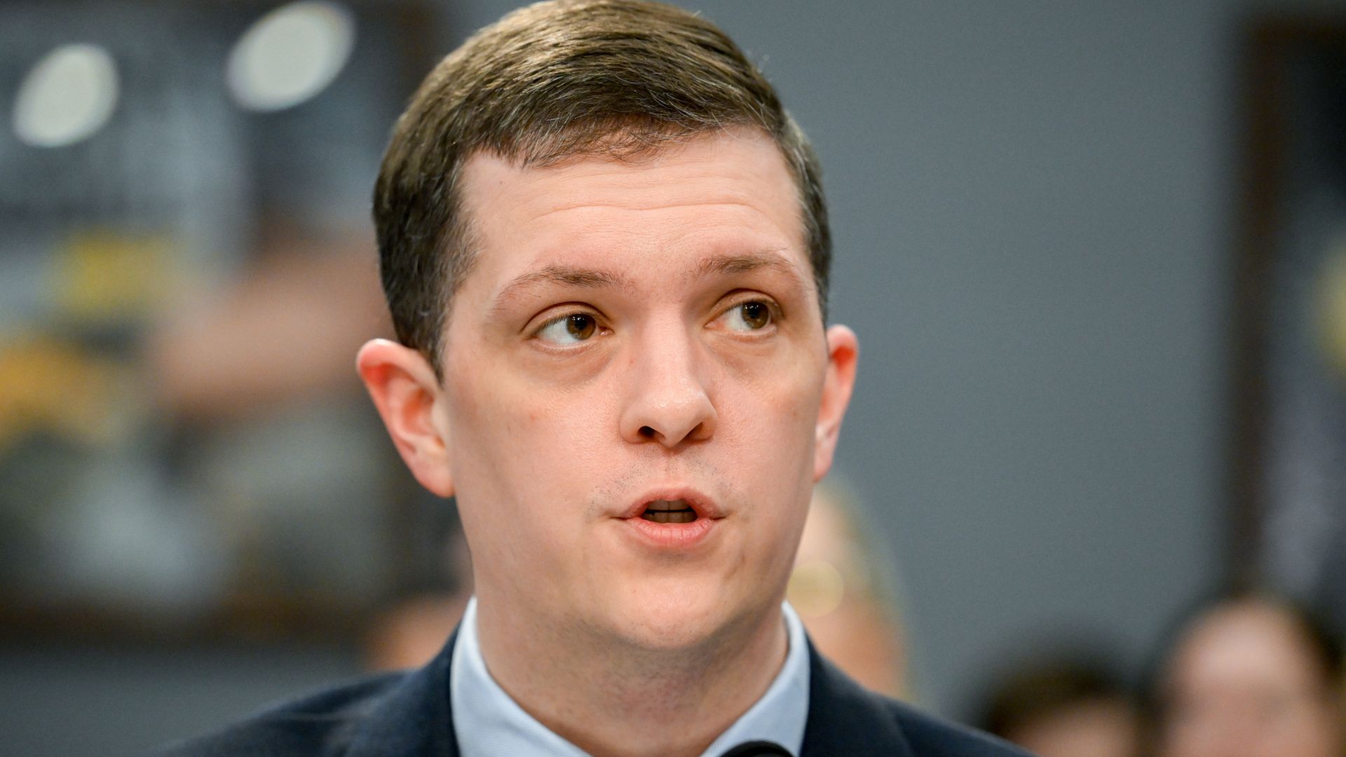A man in a tie and suit jack talking into a microphone