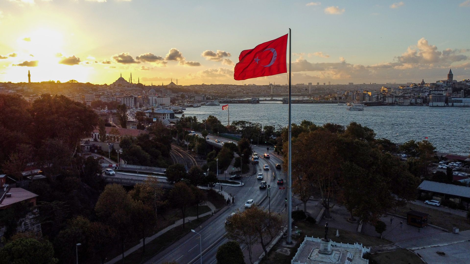 A sunset scene over the Bosphorus Strait in Istanbul, Turkey, with minarets of mosques visible in the background and dominating the skyline while traffic moves on coastal roads in the foreground