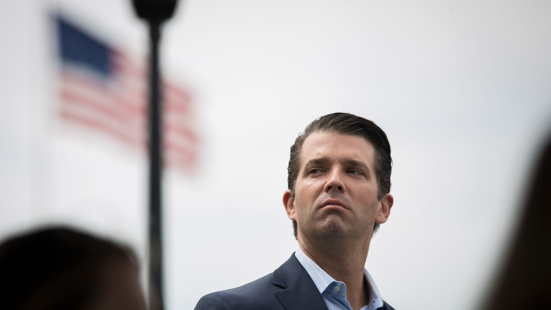 Trump Jr. looks off to the side. An American flag is in the background