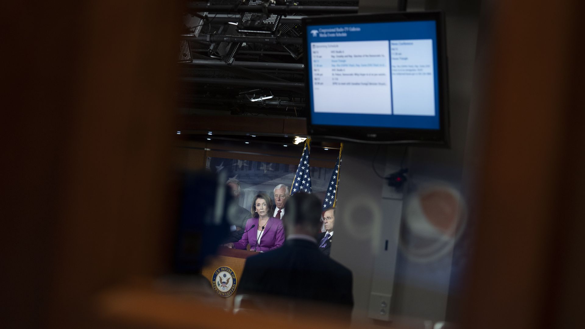 In this image, Democratic leaders stand on stage in the background of a blurred camera shot. They are standing underneath a presentation screen.